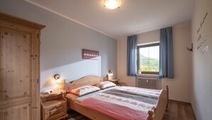 Un dormitorio con cama de madera, mesitas de noche, una ventana con cortinas, un radiador y una lámpara fijada a la pared.