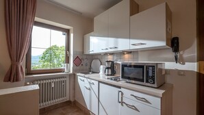 Una cocina compacta con armarios blancos, microondas integrado y ventana con vistas a zonas verdes.