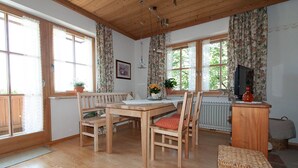 A cozy room with a wooden dining table, chairs, a wicker ottoman, and a radiator. - Vacation apartment with south-facing balcony (Riedering)