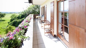 A balcony with a view of a green landscape, wooden furniture, and a large window. - Vacation apartment with south-facing balcony (Riedering)