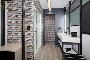 A modern bathroom with a large mirror, a white sink, and a shower area. - Aloft by Marriott Omaha Aksarben Village (Omaha)