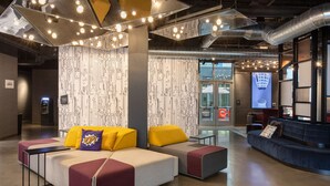 A modern lounge area with seating arrangements, a digital screen, and a patterned wall. - Aloft by Marriott Omaha Aksarben Village (Omaha)
