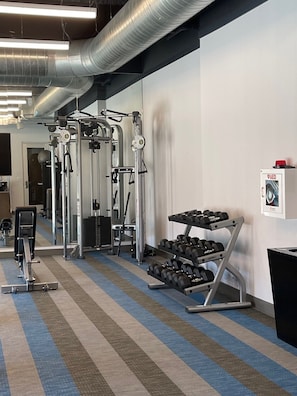 A gym with exercise equipment, a dumbbell rack, and a wall-mounted AED box.