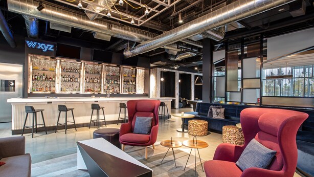 A modern bar area with a neon sign, seating arrangements, and a bar counter with various bottles. - Aloft by Marriott Omaha Aksarben Village (Omaha)