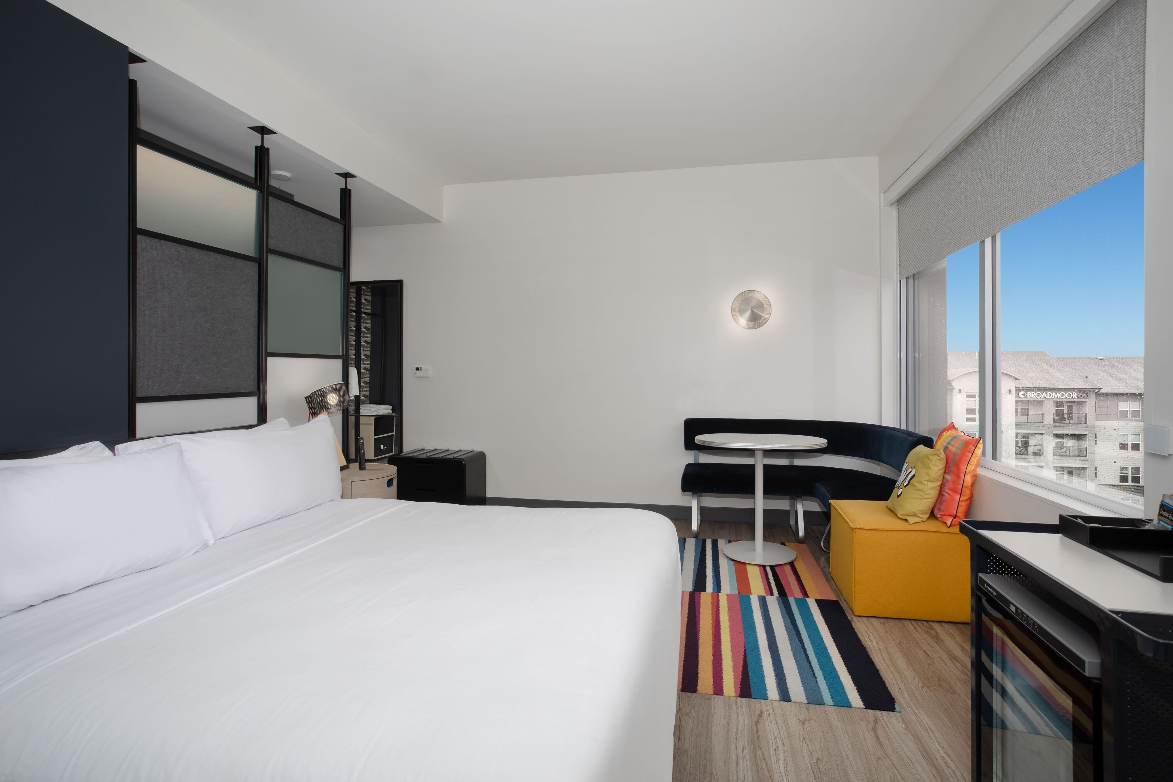 A hotel room with a large bed, a small desk, a chair, a table, and a view of the city.