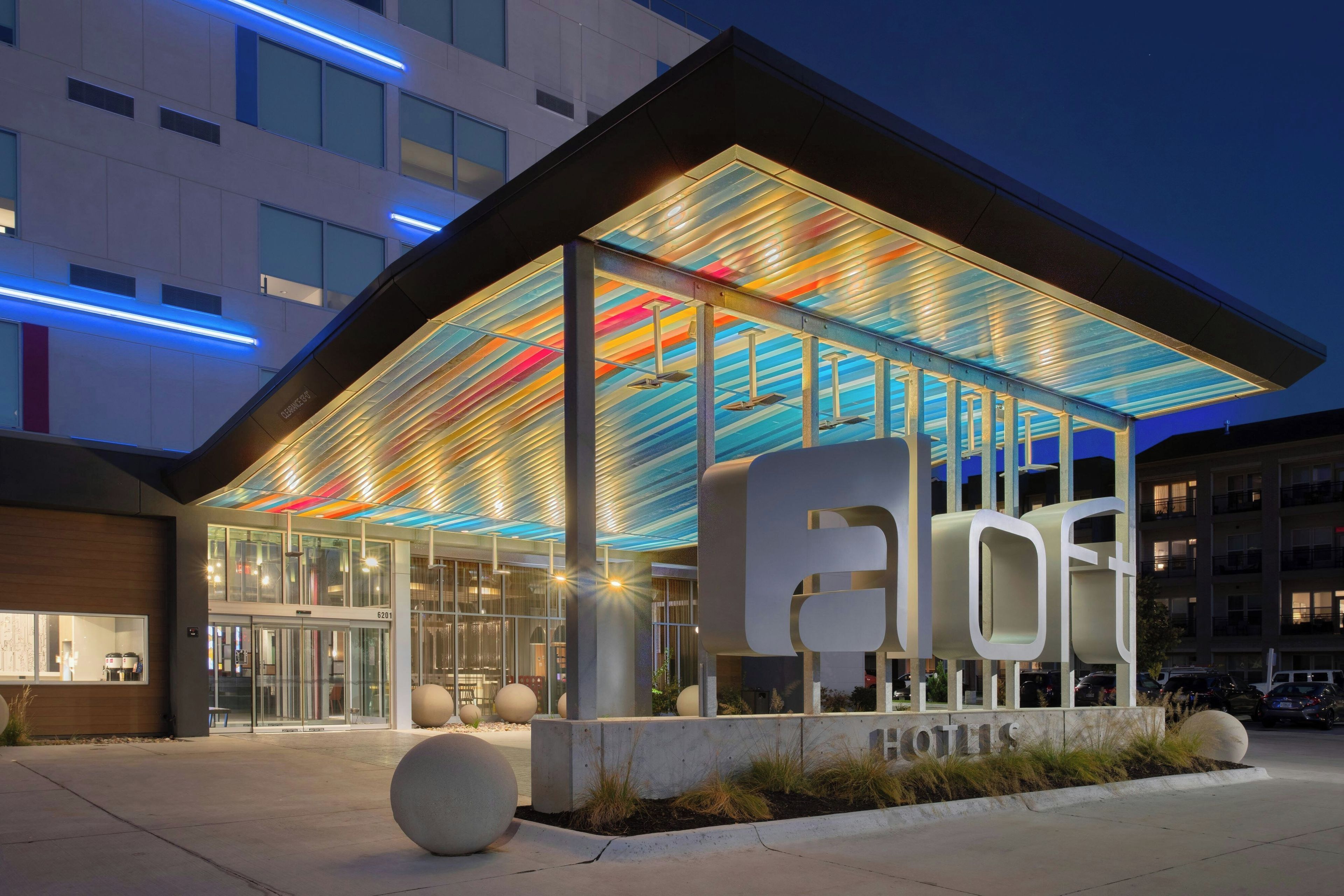 A hotel entrance with a modern design, featuring a glass facade and a colorful ceiling.