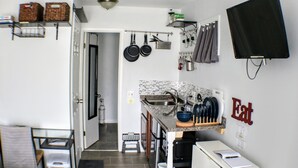 Eine kompakte Küche mit Spüle, Herd und hängenden Töpfen. Ein Fernseher ist an der Wand befestigt und eine Tür führt in einen weiteren Raum.