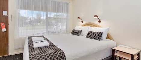 Habitación de hotel con una cama grande, una mesita de noche, una ventana con cortinas translúcidas y vistas al exterior.