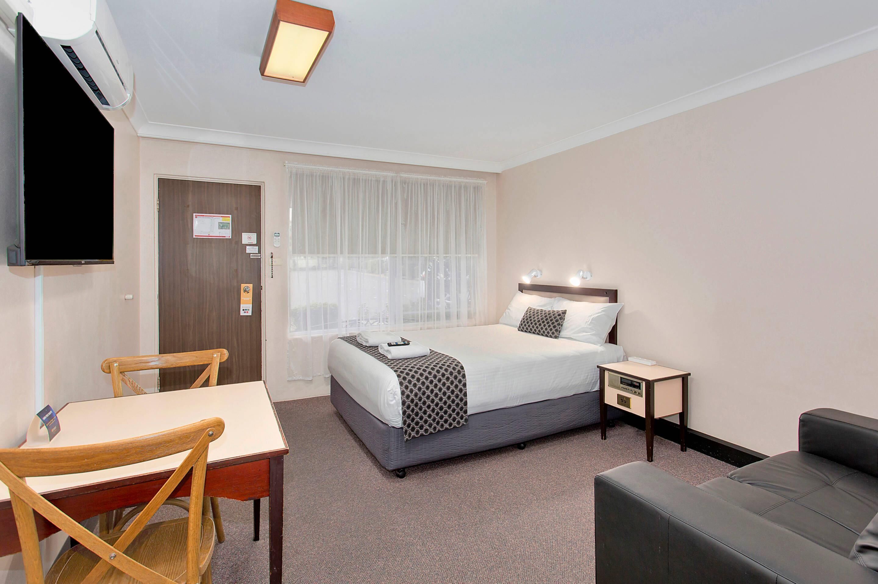 A hotel room with a bed, a desk, a chair, a TV, a bedside table, and a couch.