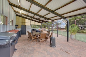 Une terrasse extérieure équipée d’un barbecue, d’une table à manger, de chaises et d’une poubelle.