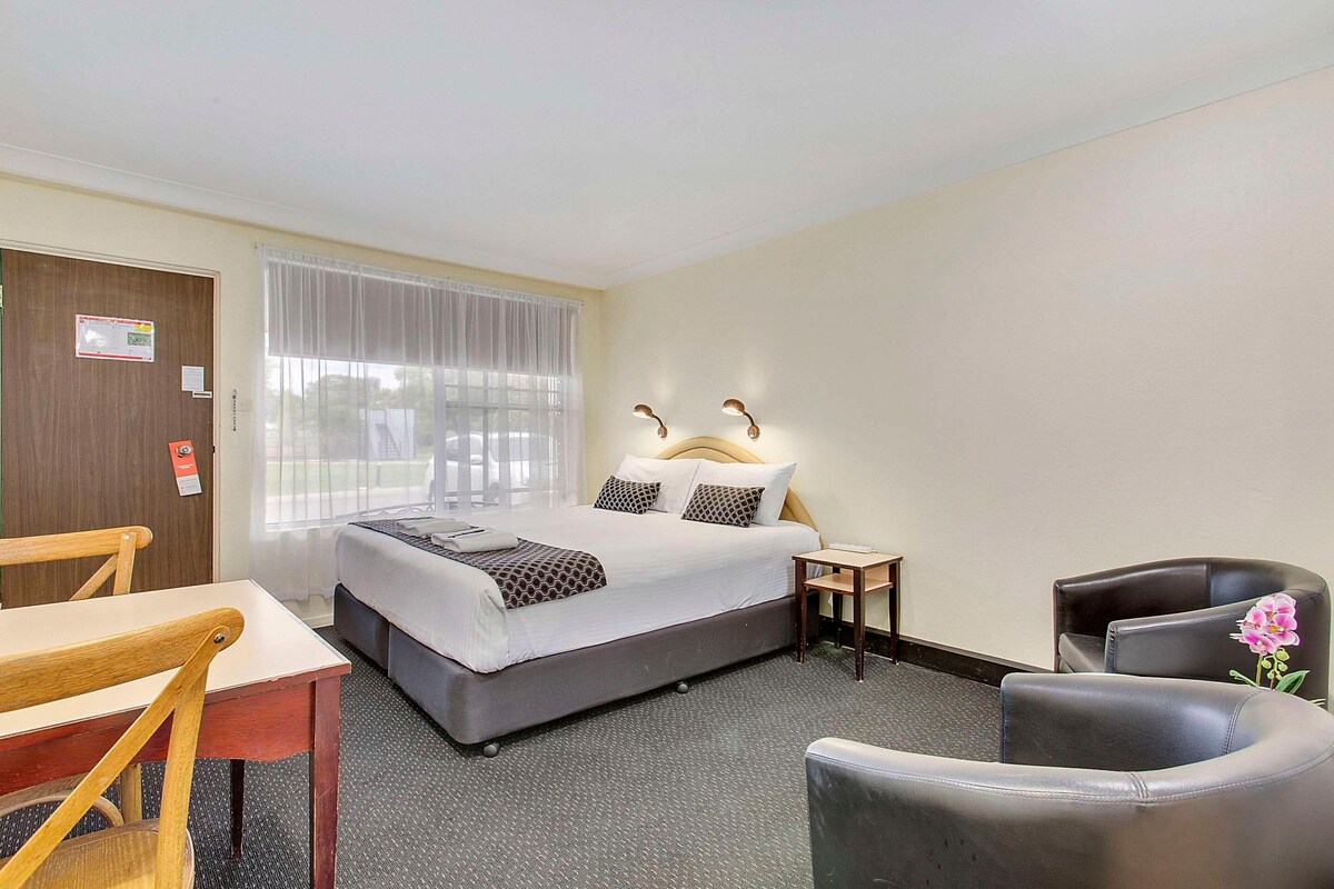 A hotel room with a bed, a desk, a chair, and a small table.