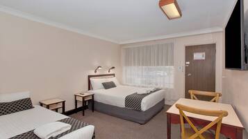 A hotel room with two beds, a desk, a chair, a TV, and a window with curtains.