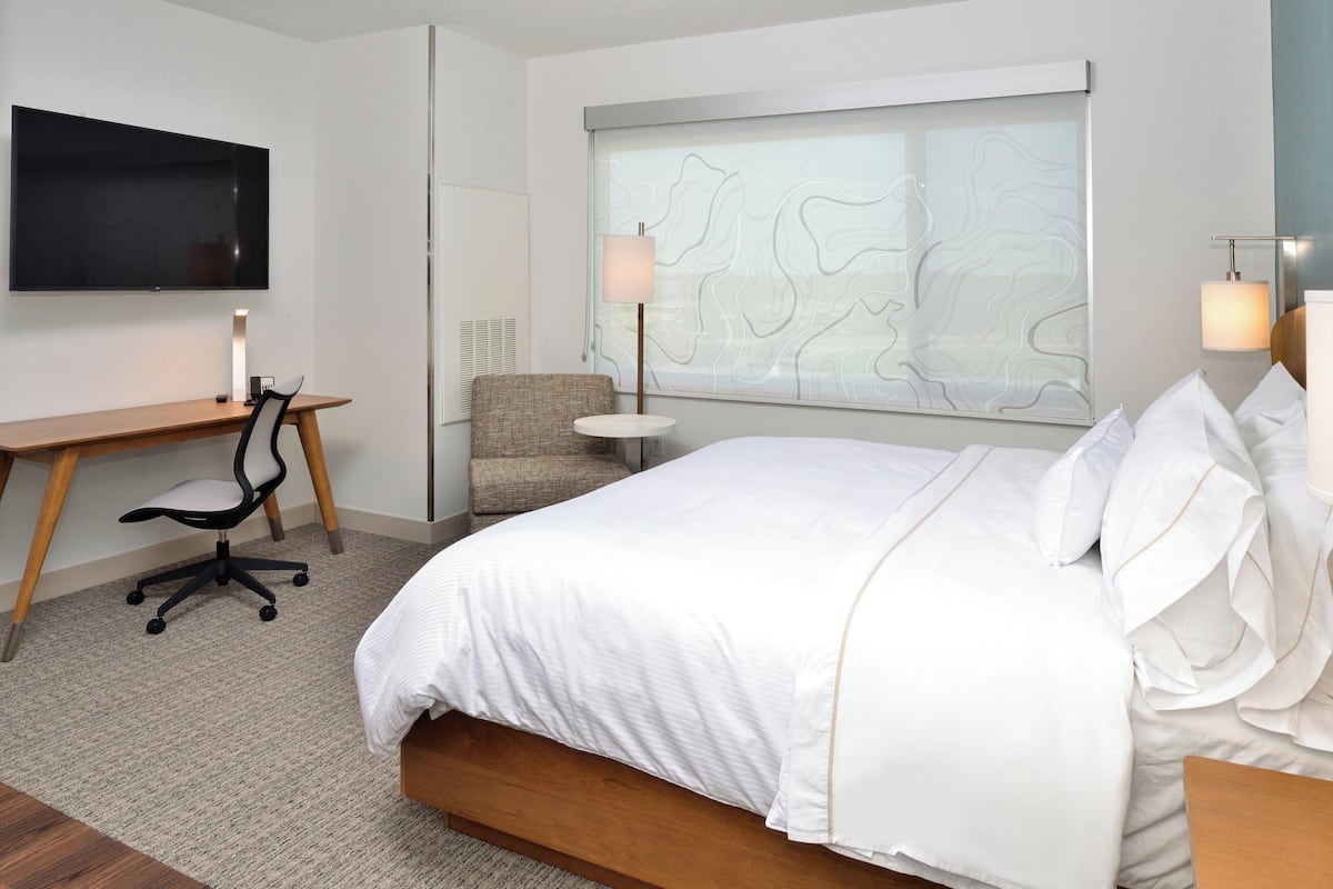 Ein Hotelzimmer mit einem großen Bett, einem Schreibtisch mit Stuhl, einem Fernseher und einem Fenster mit Landschaftsblick.