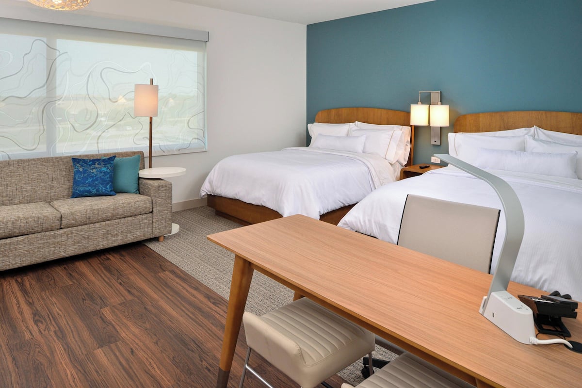 Ein Hotelzimmer mit zwei Betten, einem Sofa, einem Schreibtisch und einer Lampe.