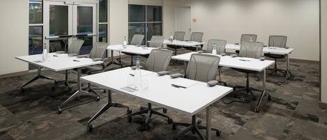 A conference room with white tables, grey chairs, and carpeted flooring.