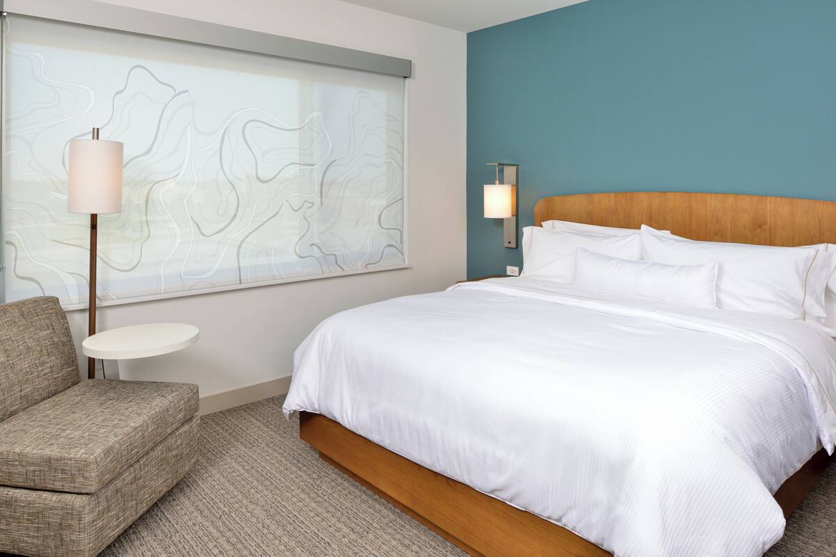 Ein Hotelzimmer mit einem Bett, einem Sessel, einem kleinen Tisch und einer Wand mit einer Karten-Musterung.