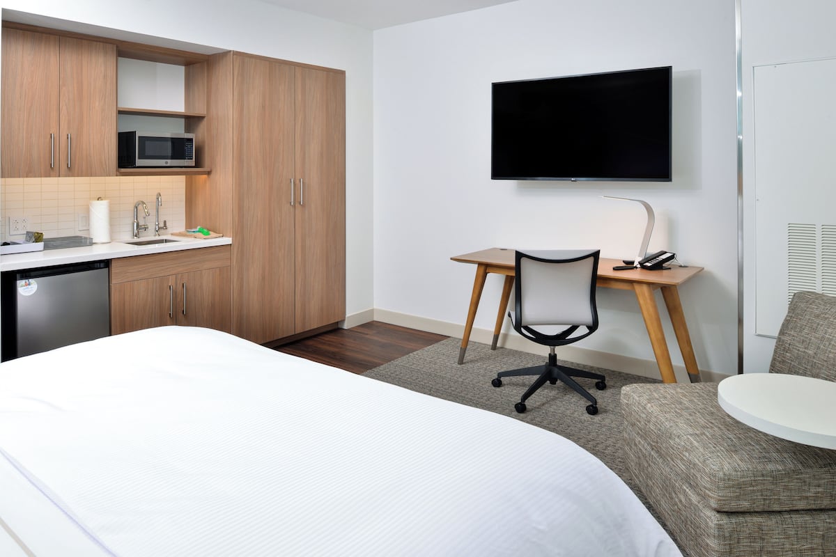 Ein Hotelzimmer mit Bett, Schreibtisch mit Stuhl, Fernseher und einer Küchenzeile.