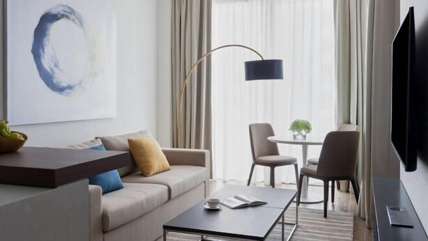 Una habitació d'hotel moderna amb un sofà, una taula de cafè, una televisió i una zona de menjador amb taula i cadires.