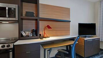 Ein kompaktes Hotelzimmer mit Küchenzeile, Schreibtisch mit Stuhl, Fernseher und roter Lampe.