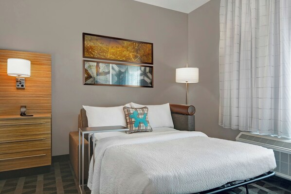 Una habitación de hotel con una cama, un aparador de madera, dos lámparas de pared y una ventana con cortinas.