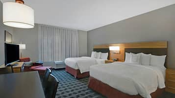 Una habitación de hotel con dos camas, un escritorio, una silla, un televisor y una lámpara.