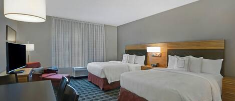 Una habitación de hotel con dos camas, un escritorio, una silla, un televisor y una lámpara.