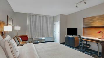 A hotel room with a large bed, a desk with a computer, a TV, and a window with curtains.
