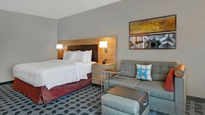 A hotel room with a bed, a sofa, a nightstand, and a wall-mounted lamp. - TownePlace Suites by Marriott Jacksonville East (Jacksonville)