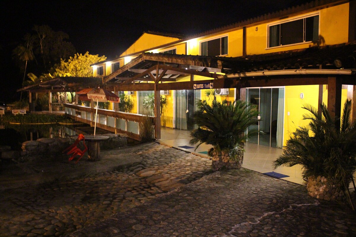 Entrada de hotel con un camino de piedra que conduce a una zona cubierta, donde se muestra un cartel con la indicación 'Suites 1-6'.