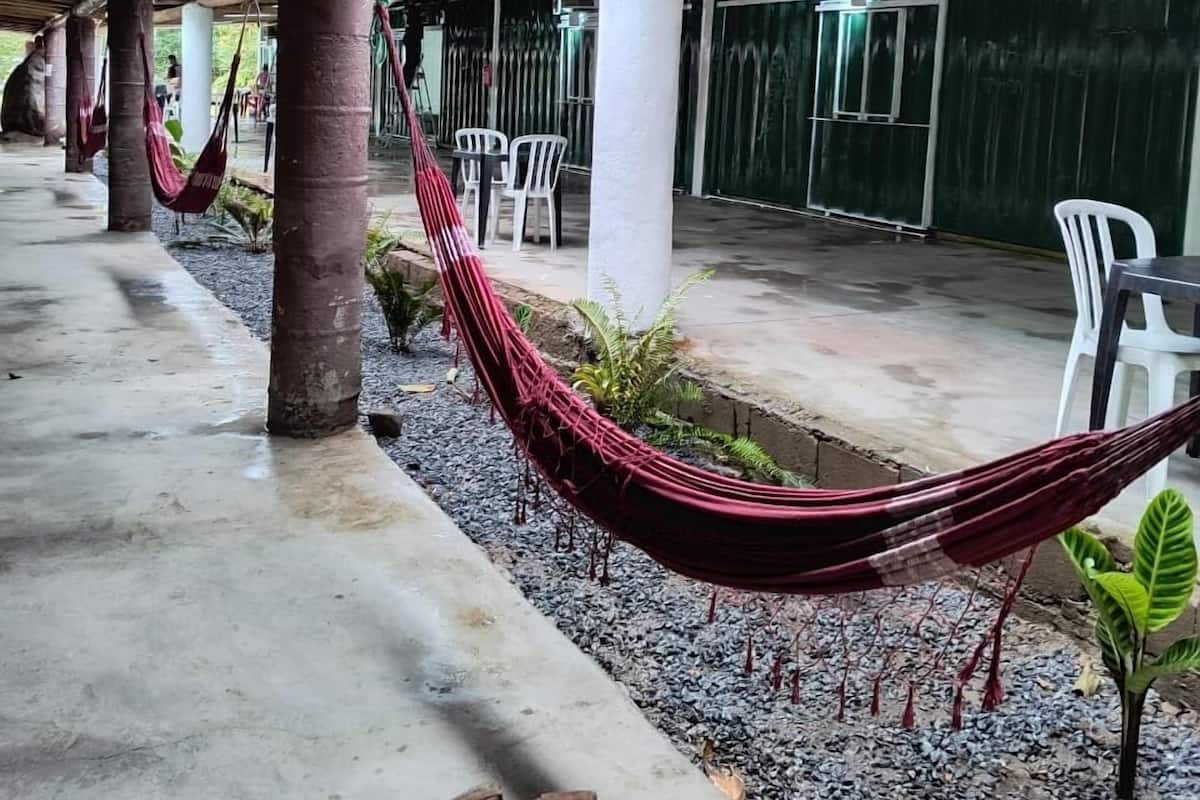 Uma área externa coberta com piso de concreto, pilares brancos e uma rede.