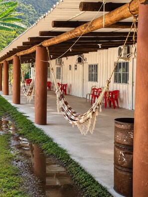 Un espace extérieur abrité, équipé de hamacs, de chaises en plastique rouge et doté d’un sol en béton.