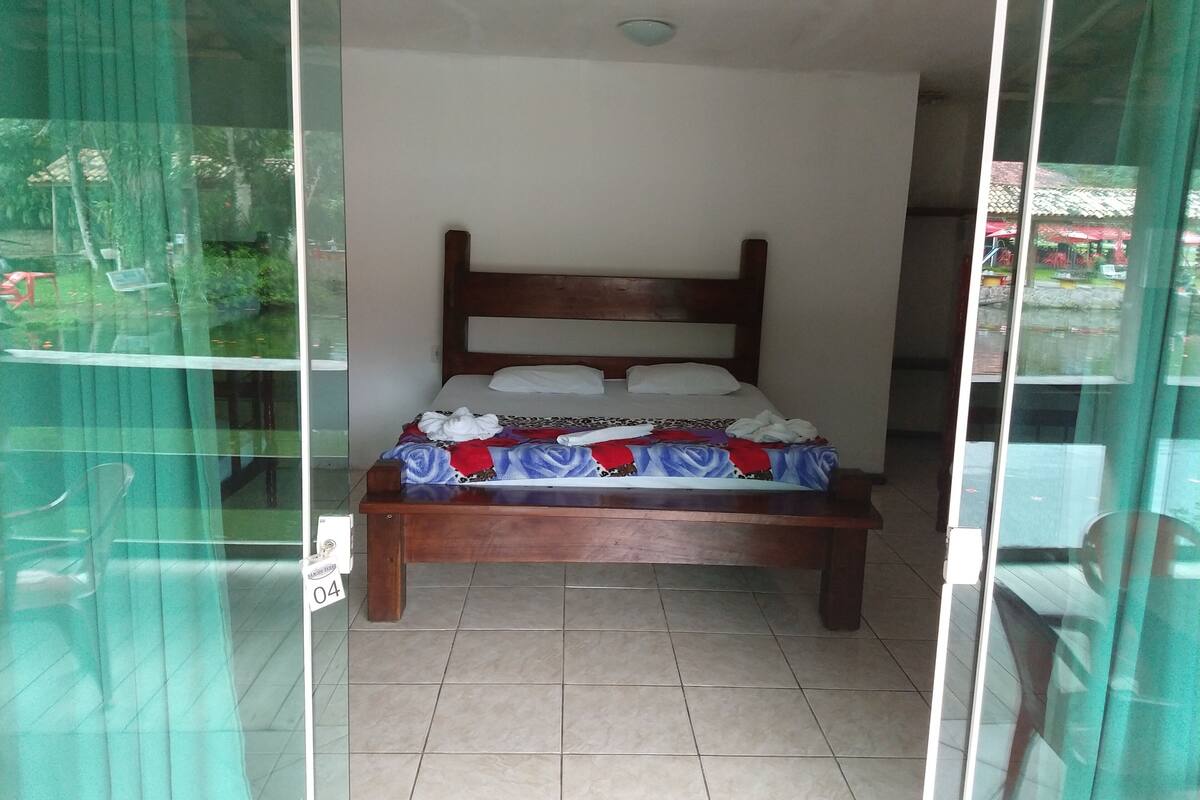 Um quarto com cama de madeira, colcha estampada e chão de azulejos.