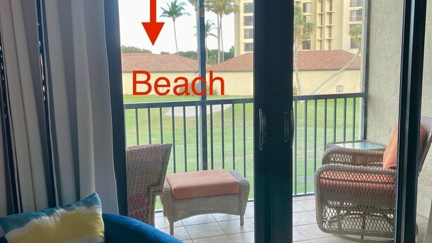 A room with a view of a beach, a sliding glass door, a blue sofa, and wicker furniture outside.