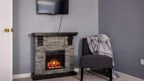 Een kamer met een stenen openhaard, een televisie erboven en een fauteuil met een plaid.