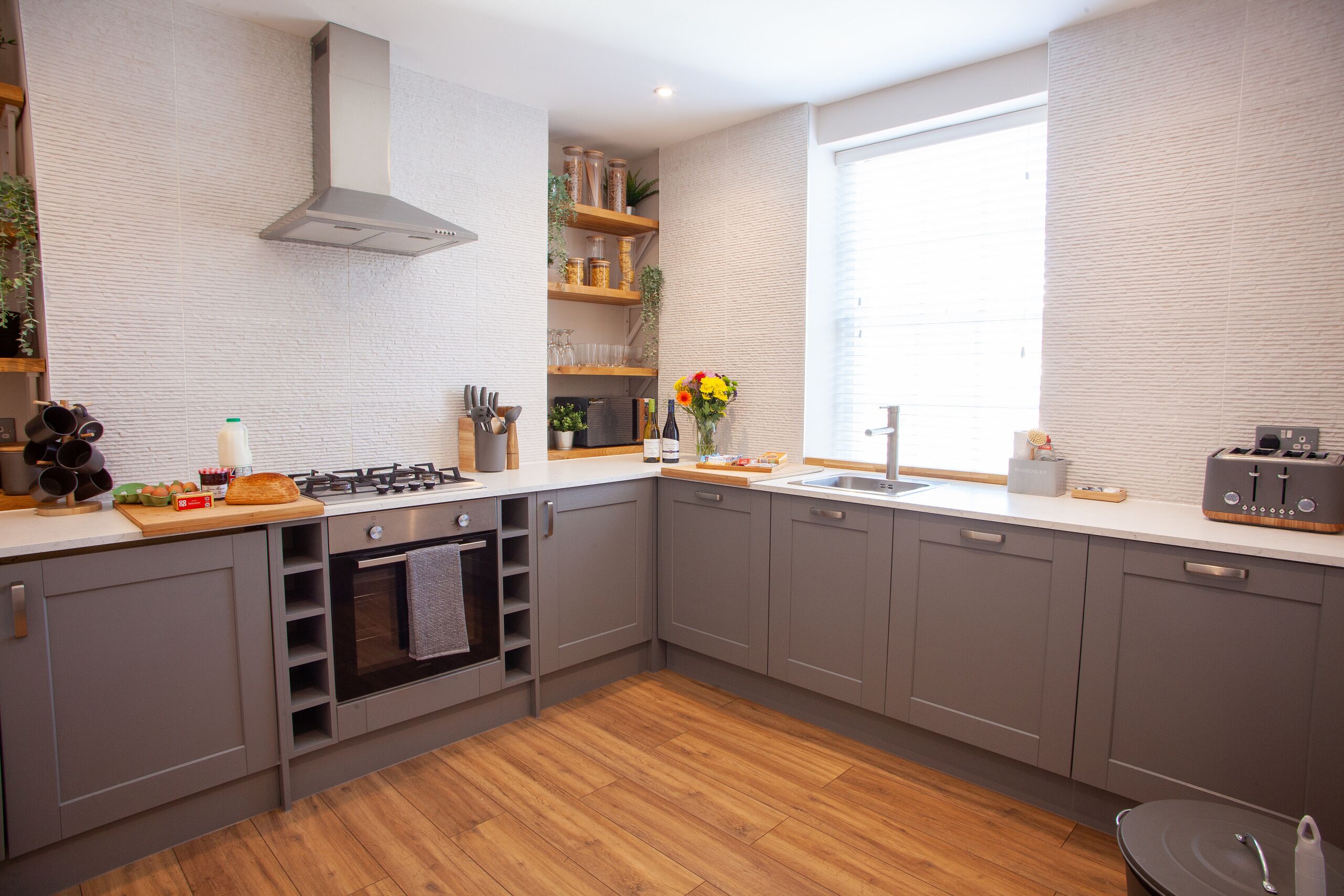 A modern kitchen with grey cabinets, a wooden countertop, a built-in oven, and a window providing natural light.