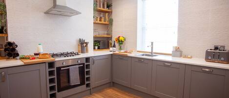 A modern kitchen with grey cabinets, a wooden countertop, a built-in oven, and a window providing natural light.