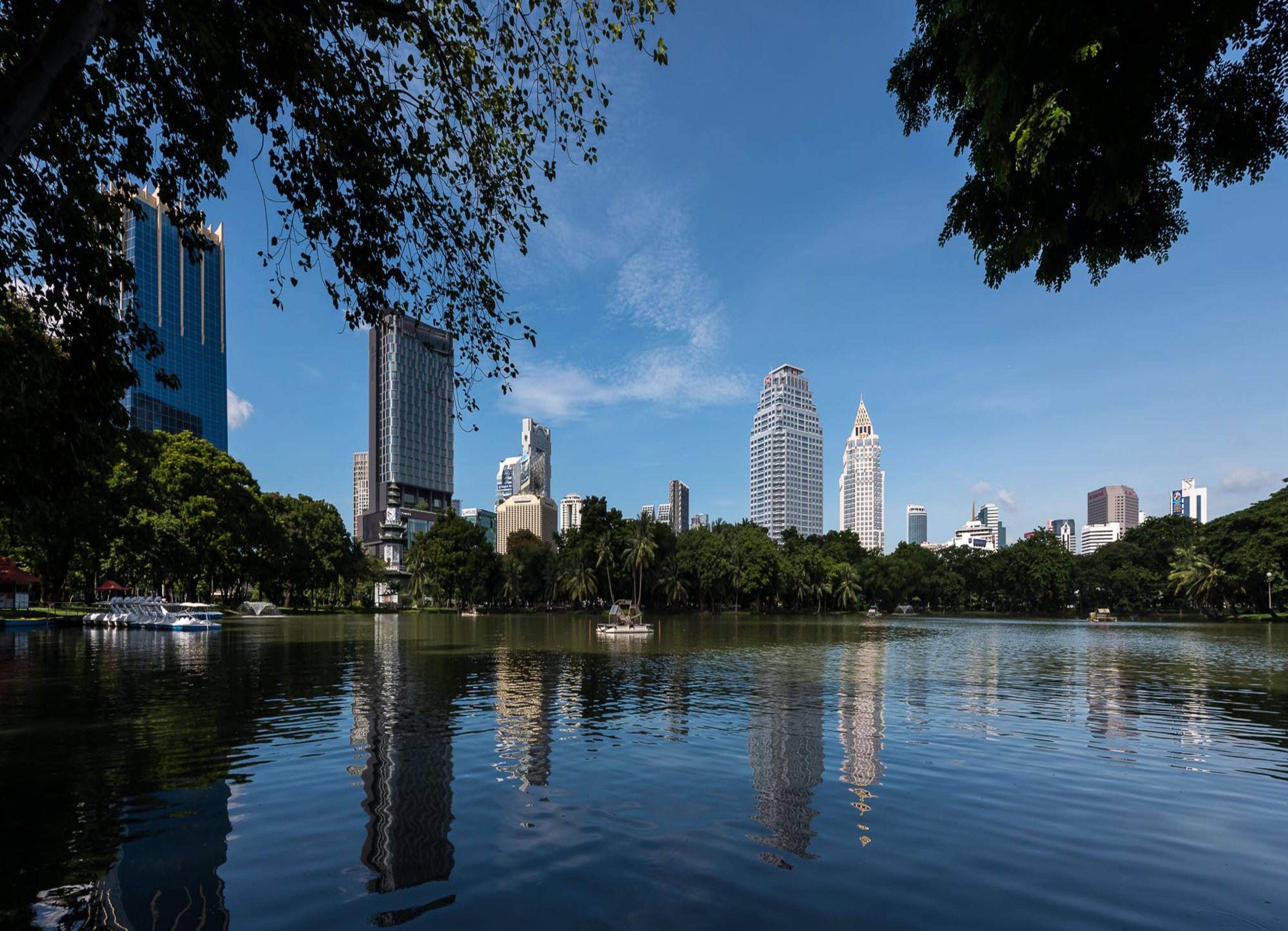 A cityscape with modern buildings, a calm lake, and lush greenery.