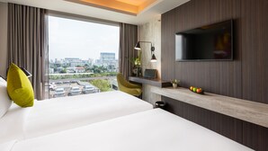 A modern hotel room with a large bed, a desk, a TV, and a city view.