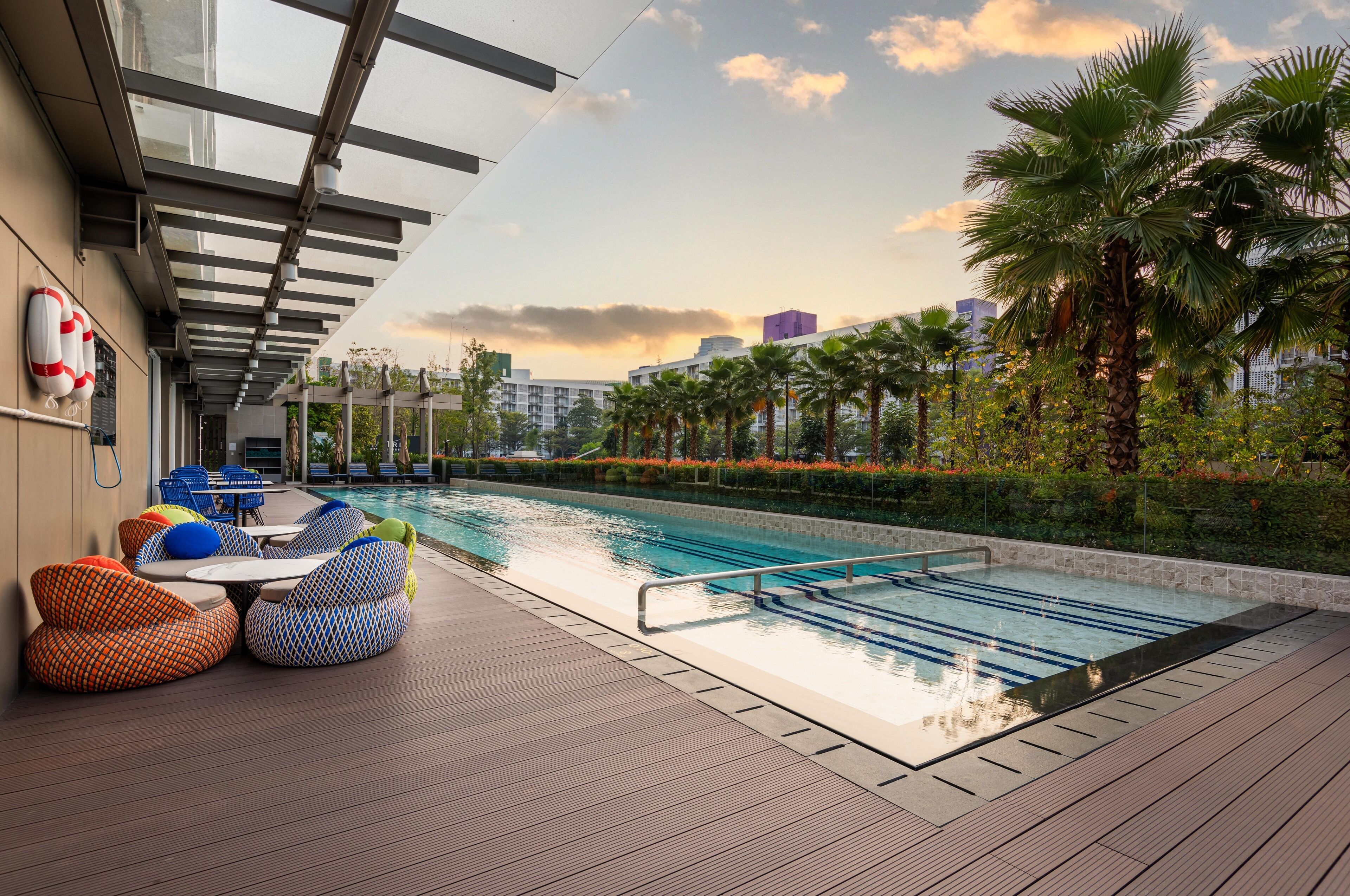 Area piscina sul tetto con poltronne prendisole e vista su palme e edifici.
