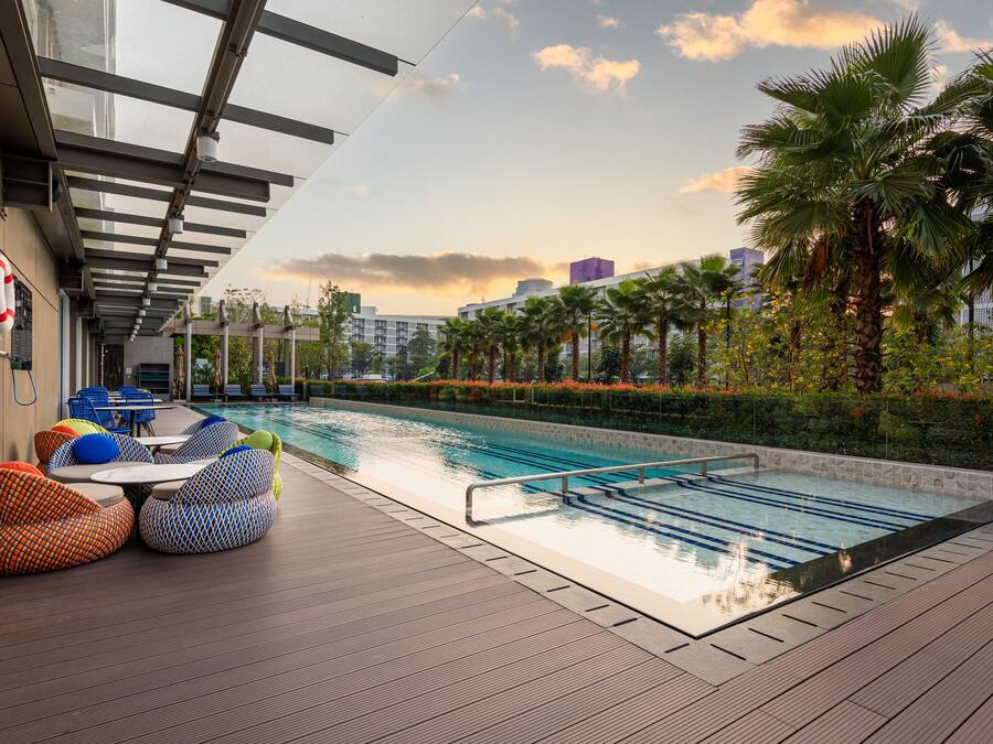 Area piscina sul tetto con poltronne prendisole e vista su palme e edifici.
