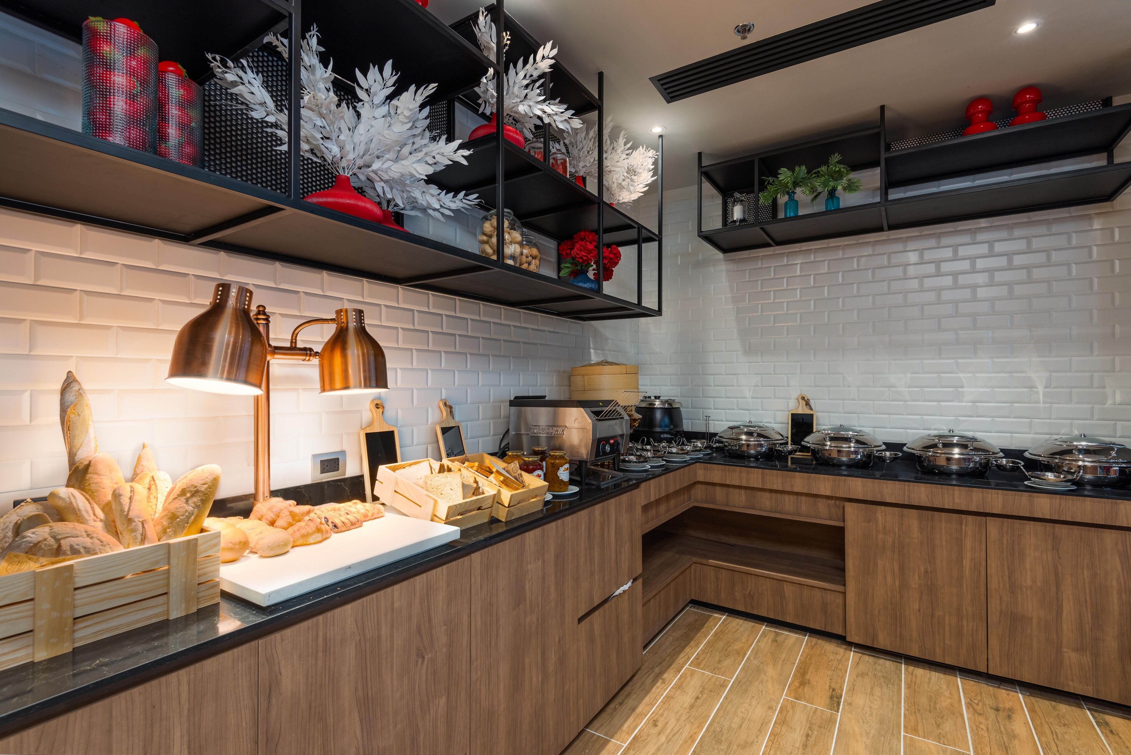 A modern kitchen with wooden cabinets, a black countertop, and a brick wall. There are shelves with decorative items and a coffee machine.