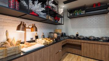 A modern kitchen with wooden cabinets, a black countertop, and a brick wall. There are shelves with decorative items and a coffee machine.