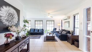 A modern living room with a dark grey sofa, a coffee table, and a large decorative piece on the wall. - Willows At The Bay, 111 Horace St - Large House with Aircon, WIFI and Boat Parking (Shoal Bay)