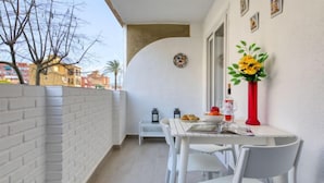 A balcony with a white table and chairs, a red vase with flowers, and a small dining table with a bottle and glasses. - Urbatenis by Interhome (Jávea)