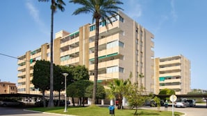 A multi-story residential building with balconies, a parking area, and palm trees. - Urbatenis by Interhome (Jávea)