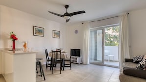 A modern living room with a sofa, a dining area with chairs and a table, a TV, and a ceiling fan. - Urbatenis by Interhome (Jávea)