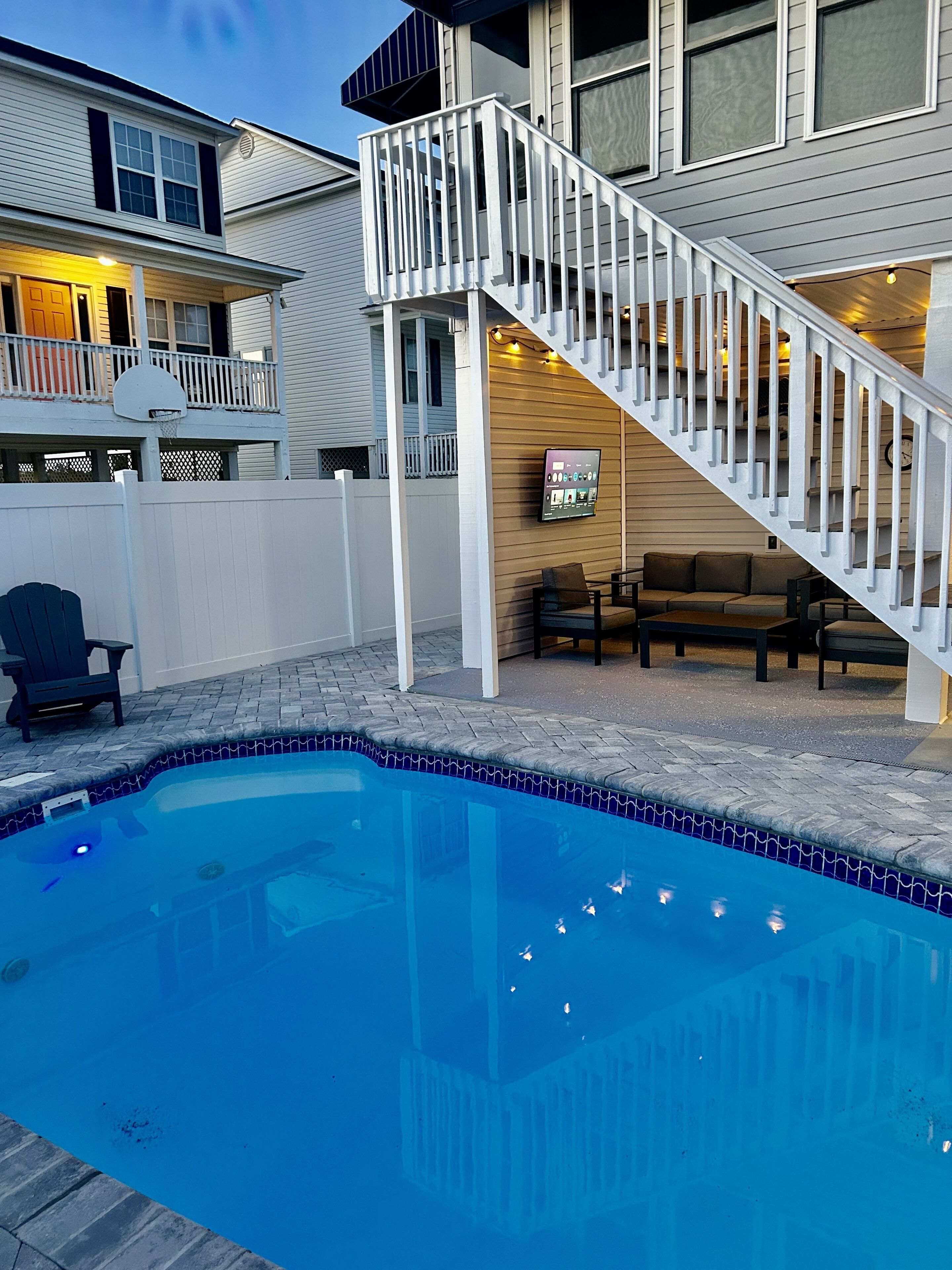 Ein Poolbereich mit klarem, blauem Wasser, einer weißen Treppe und Sitzgelegenheiten im Freien.