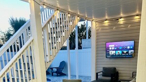 A covered outdoor patio with a TV mounted on the wall, outdoor furniture, and a white staircase.