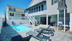 A pool area with lounge chairs, a staircase, and a covered patio.