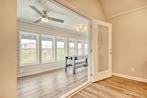Enjoy the airy feel of this room with a high ceiling and sloped roof, featuring a ceiling fan and wall-mounted light fixture.